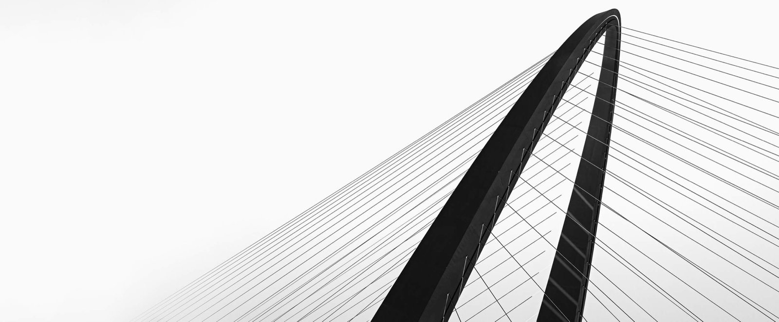 The arch and stay cables of a modern suspension bridge against a white sky