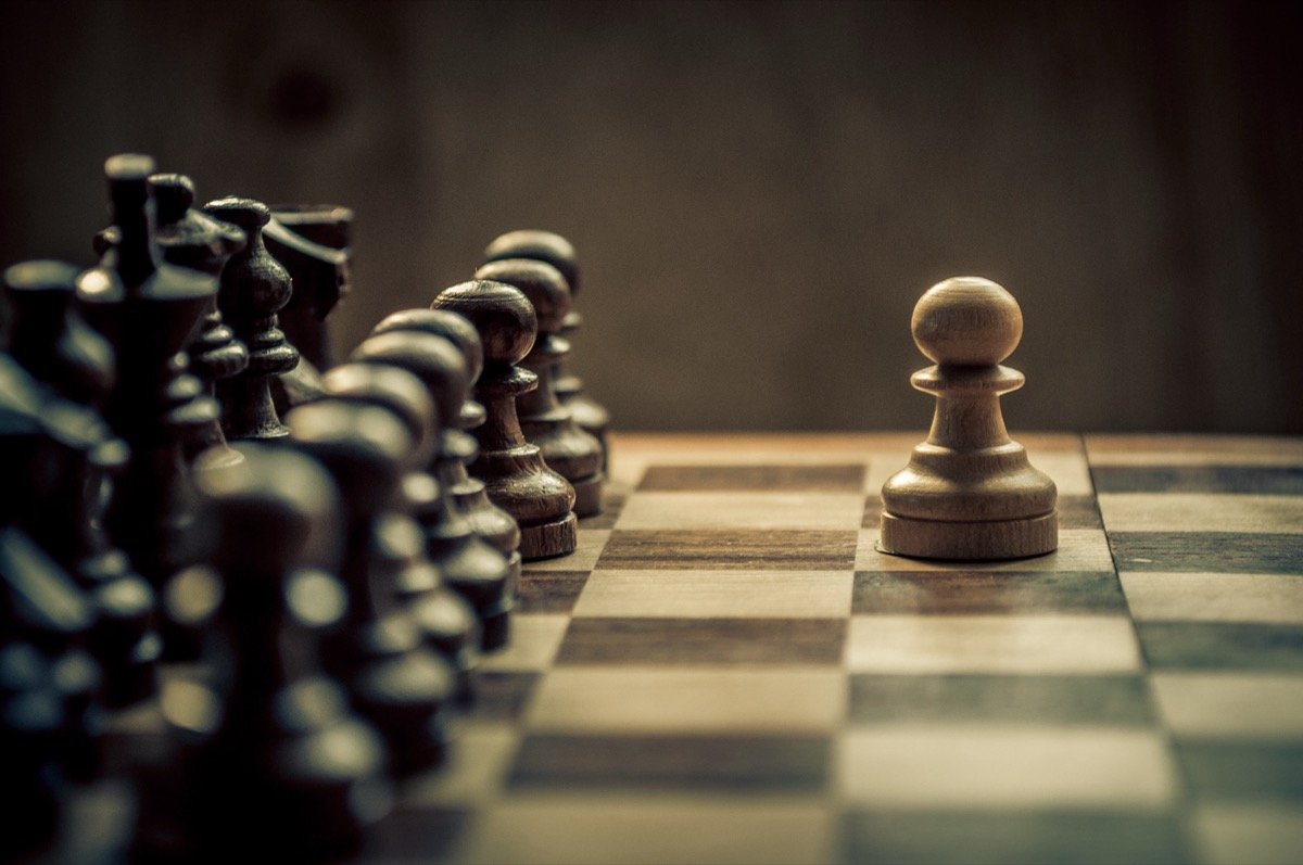 Chess pieces facing a lone pawn across the board